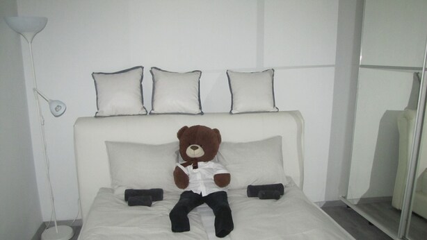 A neatly made bed with a teddy bear dressed in a white shirt and black pants sitting on it. - Cool 2-bedroom apartment with AC in Szeged (Szeged)