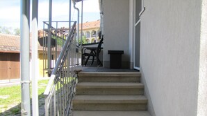 A set of concrete stairs leading to a porch with a metal railing, a black trash bin, and a table with chairs. - Cool 2-bedroom apartment with AC in Szeged (Szeged)