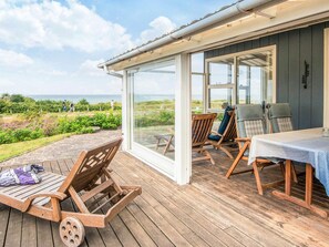 A wooden deck with a table and chairs, overlooking a garden and the sea.