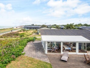 A coastal property with a glass-enclosed patio area, a wooden deck, and a view of the sea.