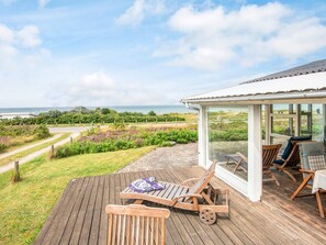 A wooden deck with outdoor furniture, a glass-enclosed patio area, and a view of the sea.