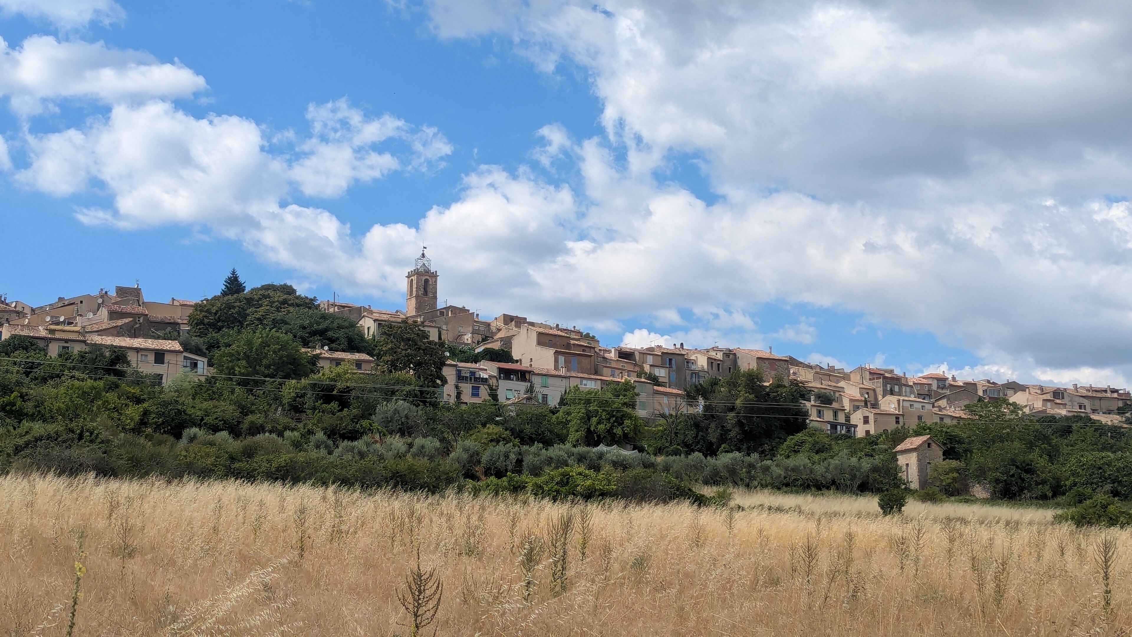 A historic town with terracotta-roofed buildings, a prominent tower, and a foreground of dry grassland.