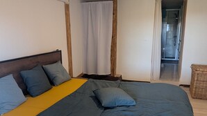 Un dormitorio con una cama grande, cabecera de madera, cortina blanca y una pequeña cesta de mimbre.
