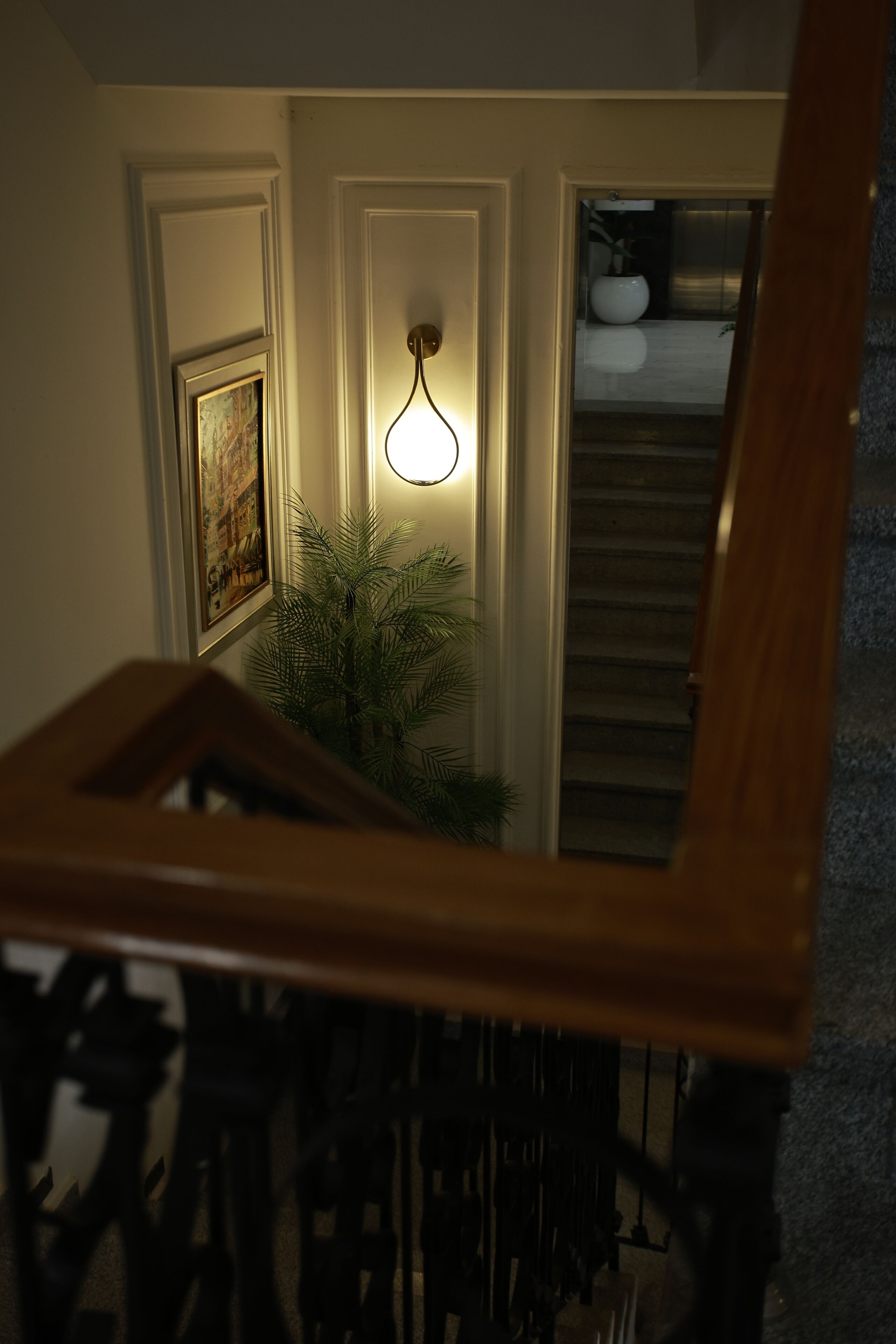 Uma escada com corrimão de madeira, luminária fixada na parede e um quadro emoldurado.