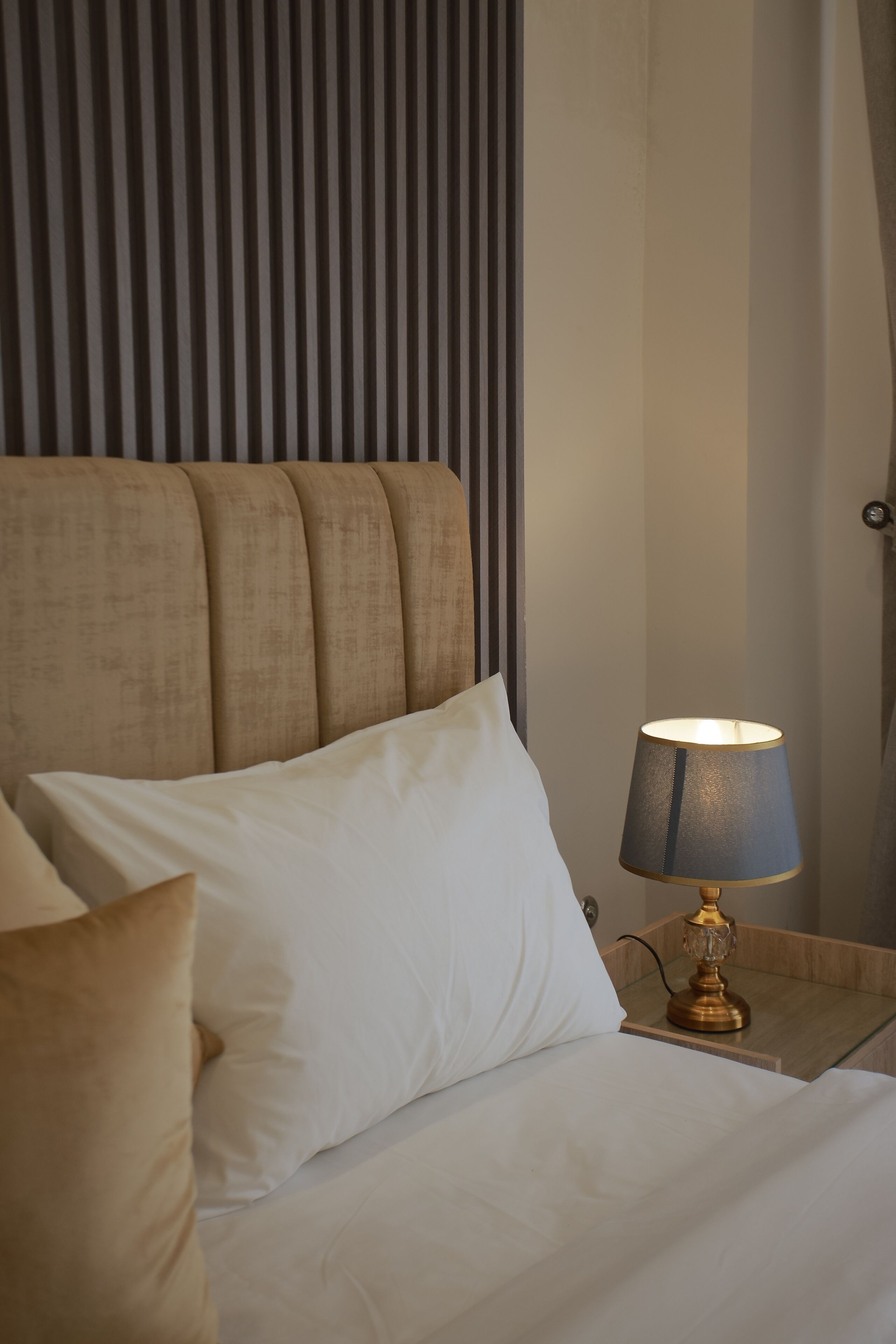 A neatly made bed with white linens and a gold-toned lamp on a bedside table.