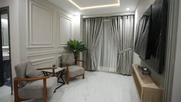 A modern living room with a flat-screen TV, two armchairs, a small table, and a potted plant.