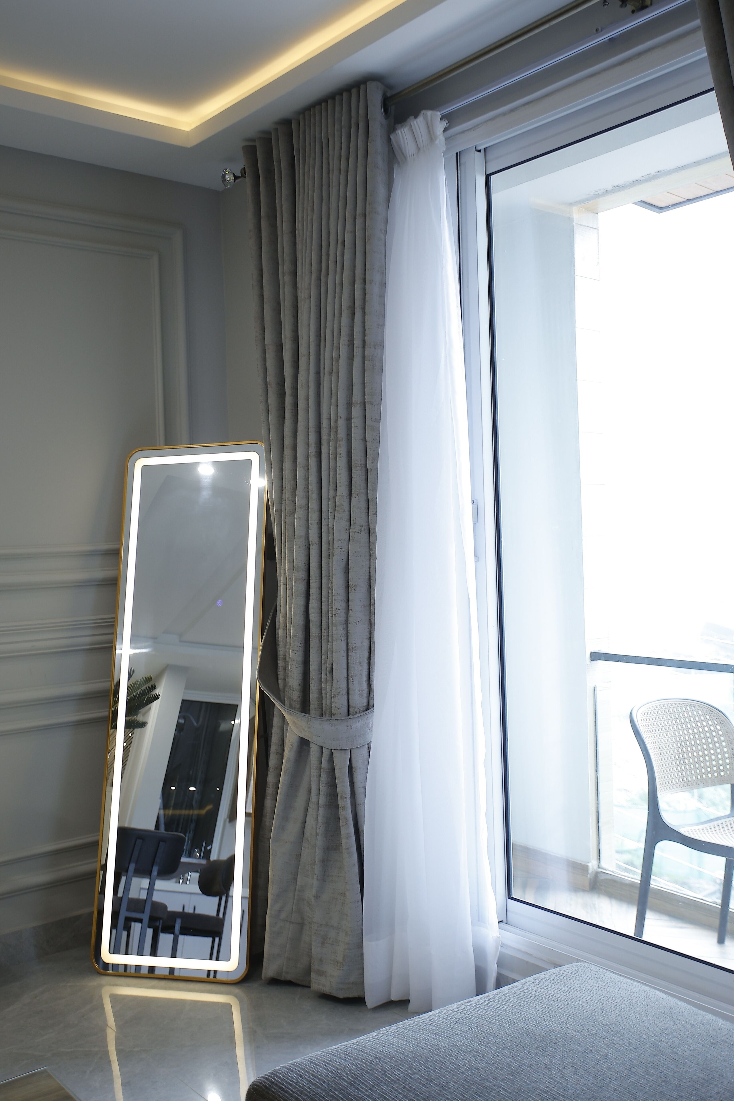 A hotel room with a large mirror, a balcony with a chair, and a view of the outdoors.