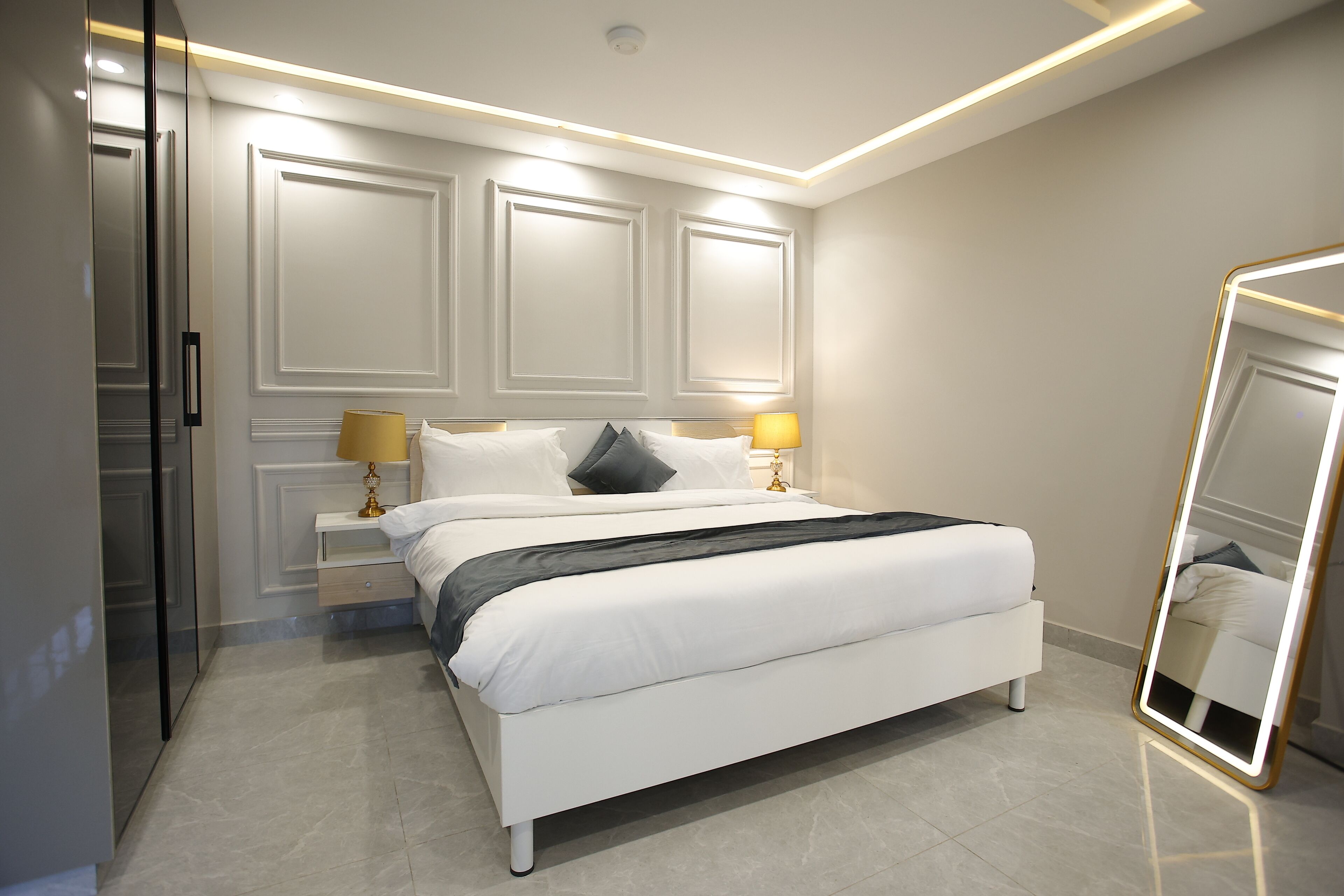 Un dormitorio moderno con una cama grande, lámparas de noche, un espejo y un armario.