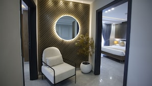 A modern hotel room with a round mirror, a white chair, a potted plant, and a bed with a nightstand.