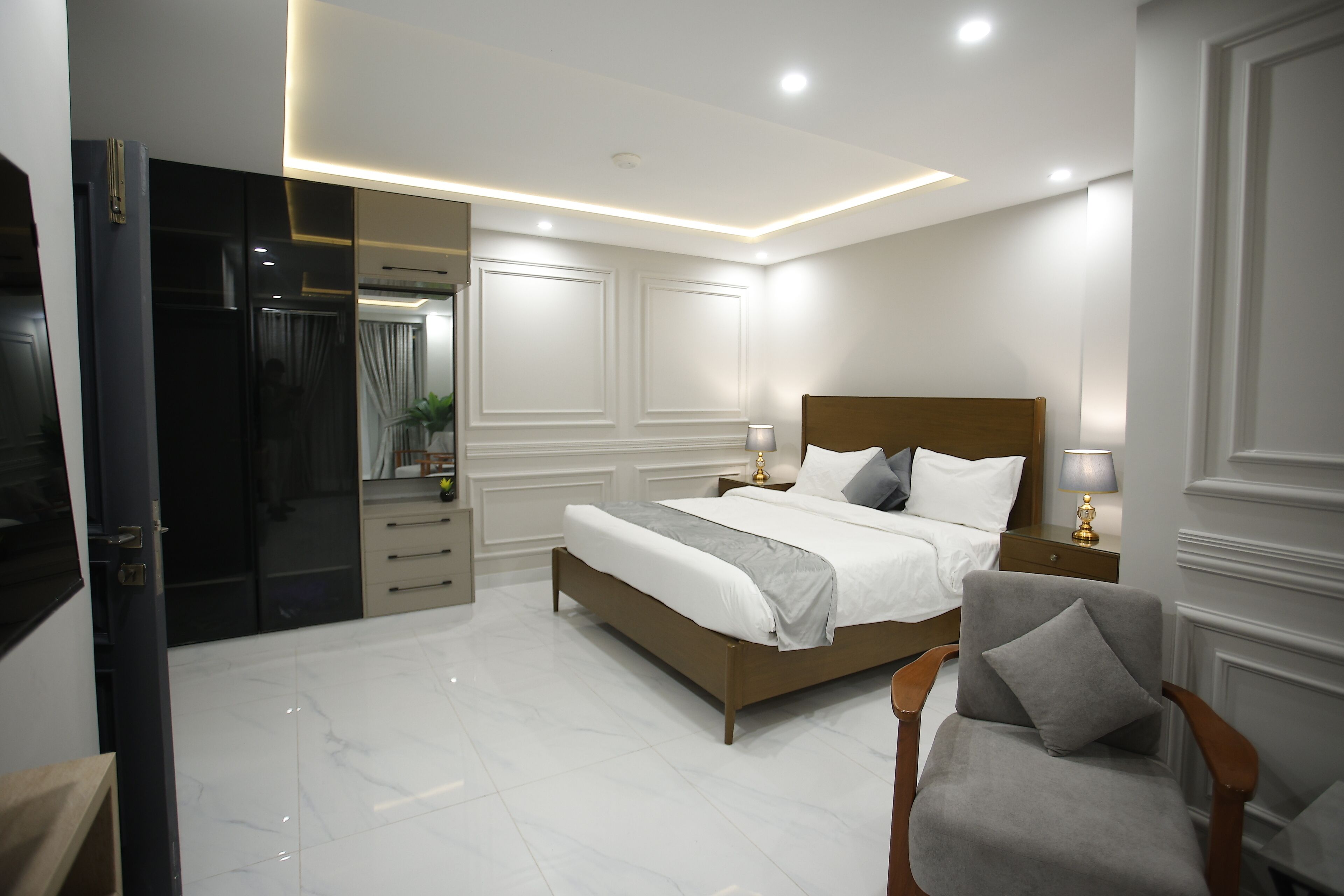 A modern bedroom with a large bed, bedside tables, a chair, and a walk-in closet.