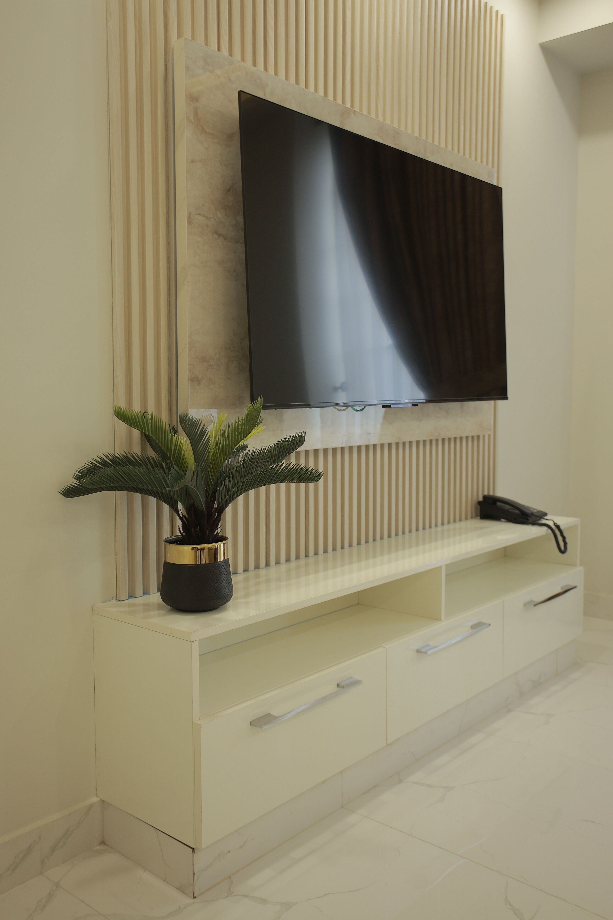 Una sala de estar moderna con un televisor de pantalla plana montado en una pared con un panel decorativo, una consola blanca con cajones y una planta en maceta.