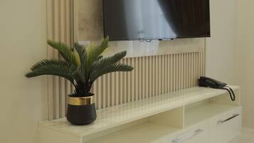Una sala de estar moderna con un televisor de pantalla plana montado en una pared con un panel decorativo, una consola blanca con cajones y una planta en maceta.