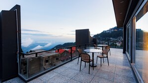 A balcony with a table and chairs, overlooking a mountainous landscape.