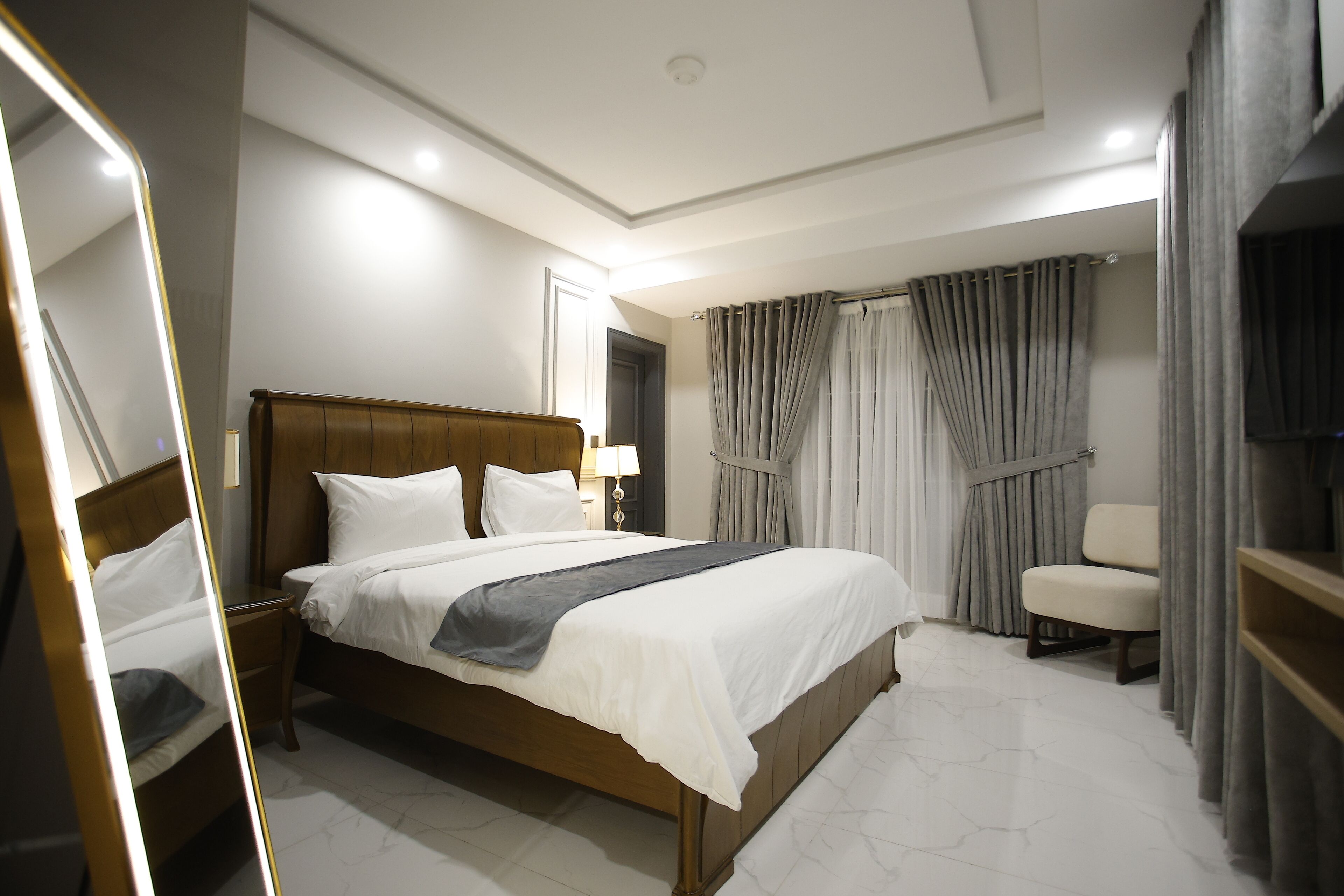 A hotel room with a large bed, a bedside table, a chair, and a TV.