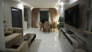 A modern living room with a sofa, coffee table, TV, fireplace, and dining area.