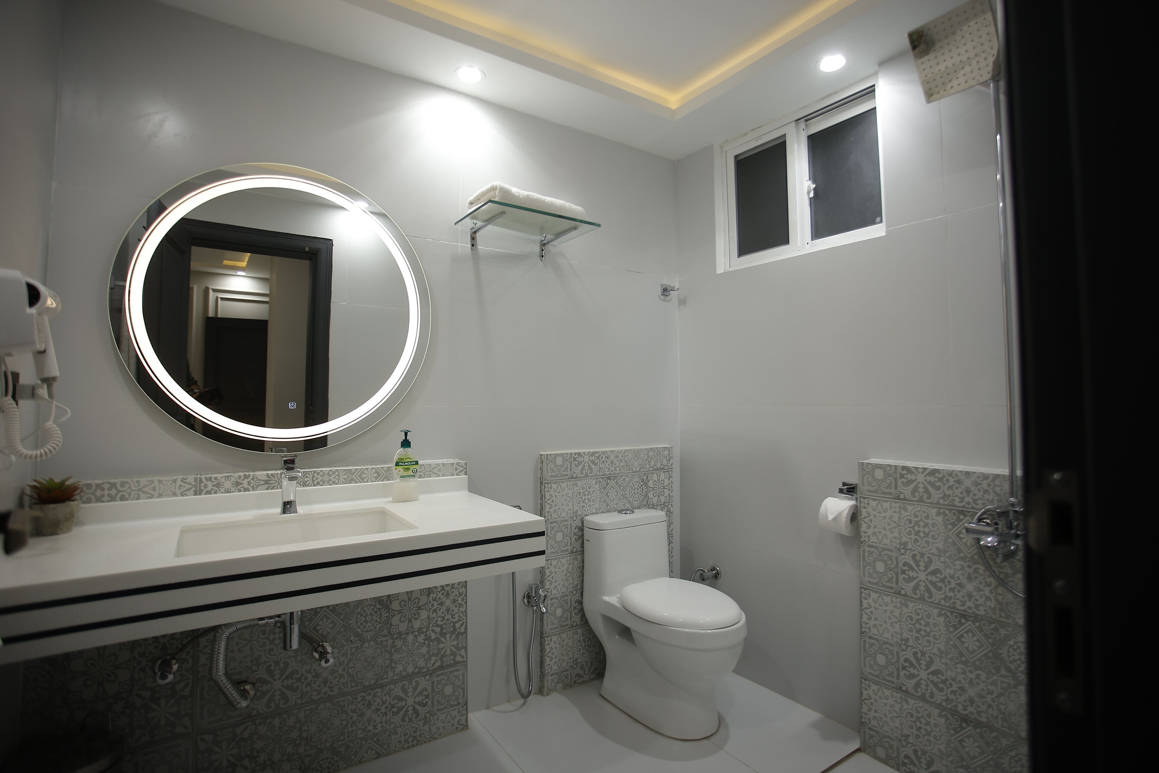 A modern bathroom with a round mirror, white sink, toilet, and shower.