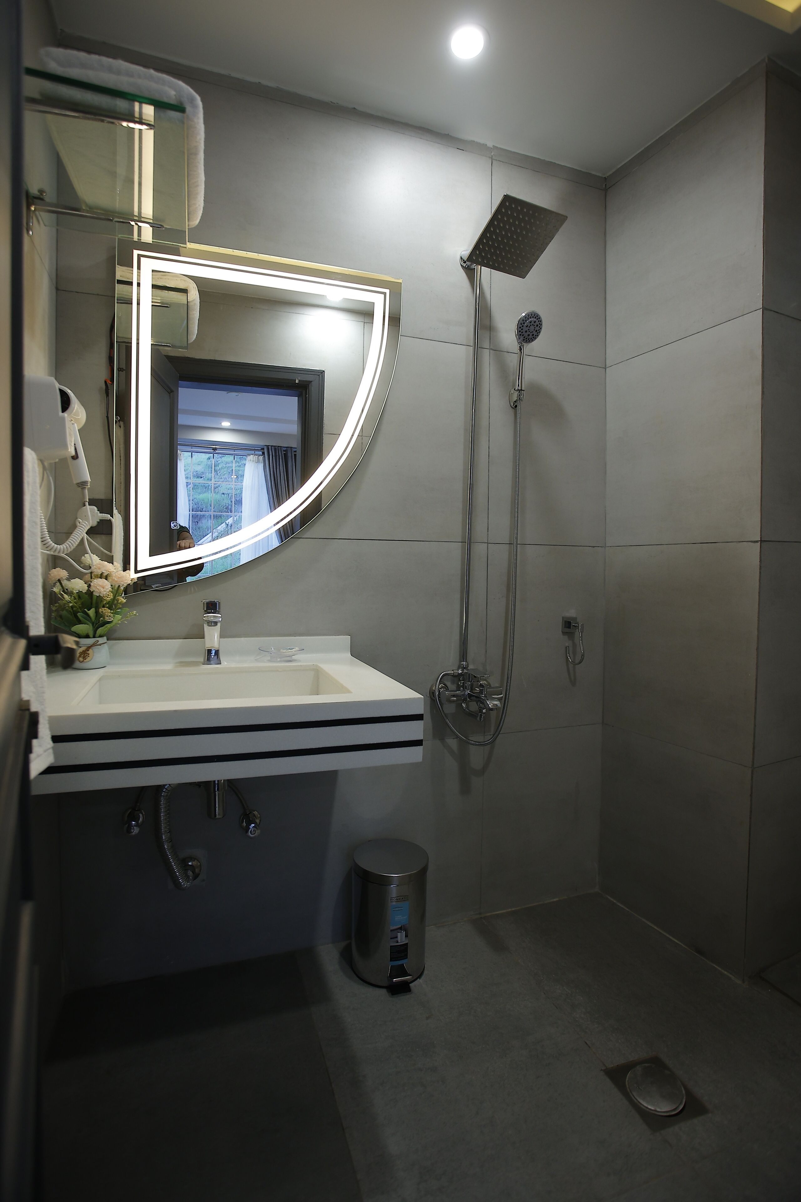 Un bagno moderno con un lavandino bianco, uno specchio con illuminazione integrata, un soffione doccia e un cestino.