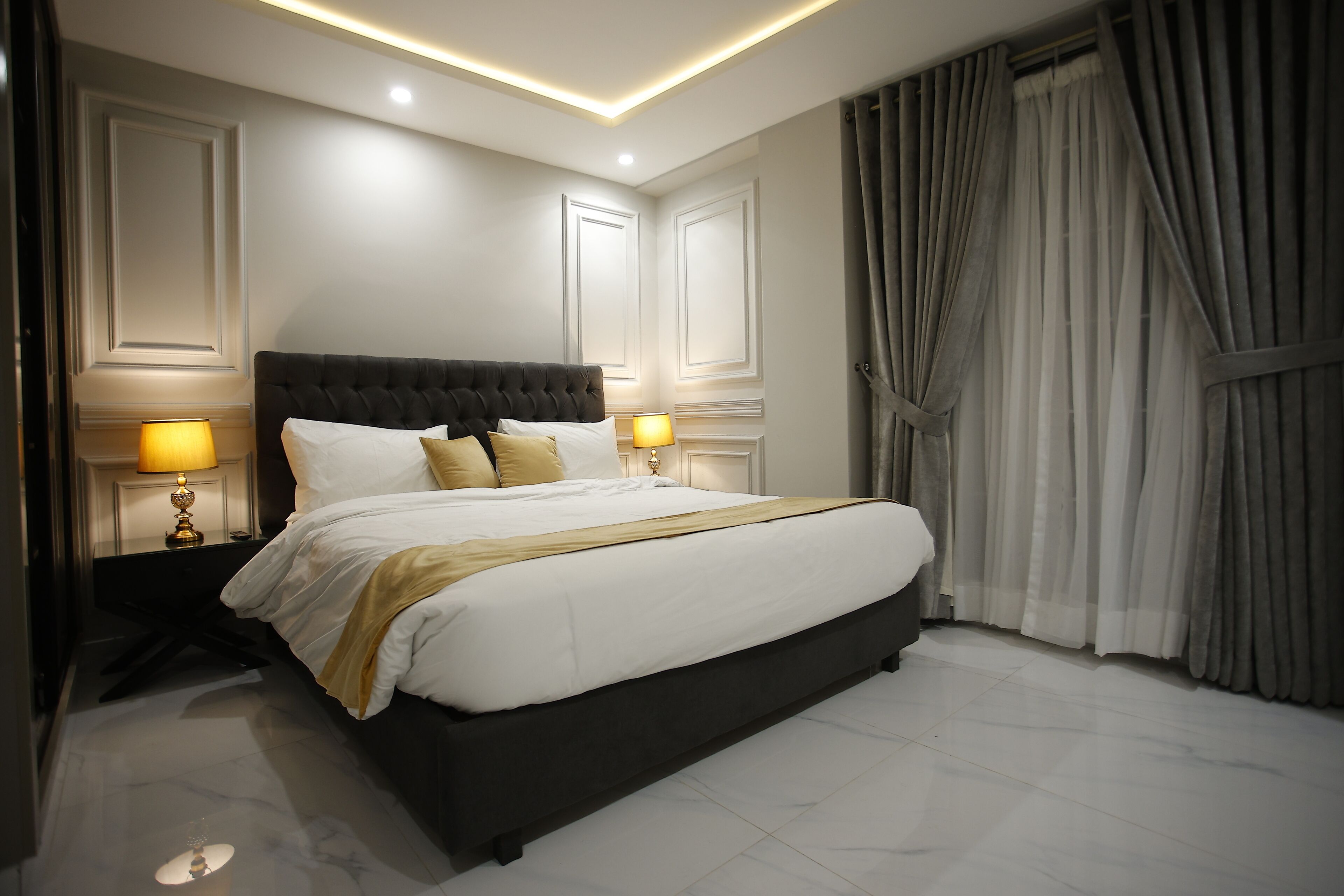 A modern hotel room with a large bed, two bedside lamps, and a large window with curtains.