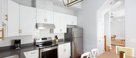 A modern kitchen with white cabinets, stainless steel appliances, and a wooden dining table.