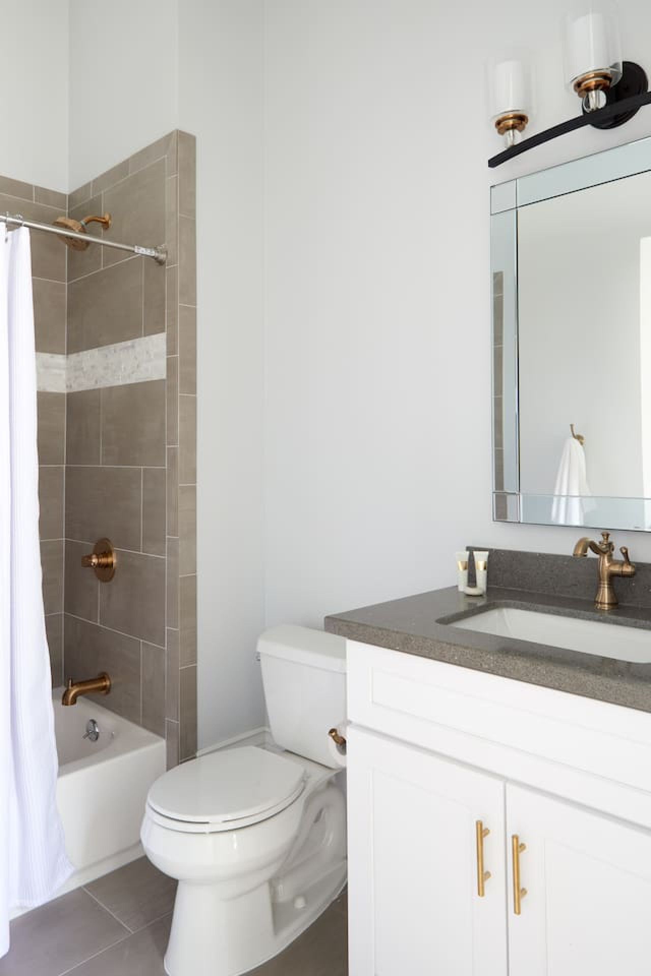 A bathroom with a shower, toilet, sink, and a mirror.