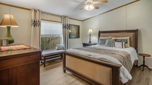 A bedroom with a wooden bed, bedside tables, a bench, a desk with a lamp, and a ceiling fan. - Nature-filled escape near Seneca Falls—sleep 8, explore wineries, and unwind in total comfort. (Seneca Falls)