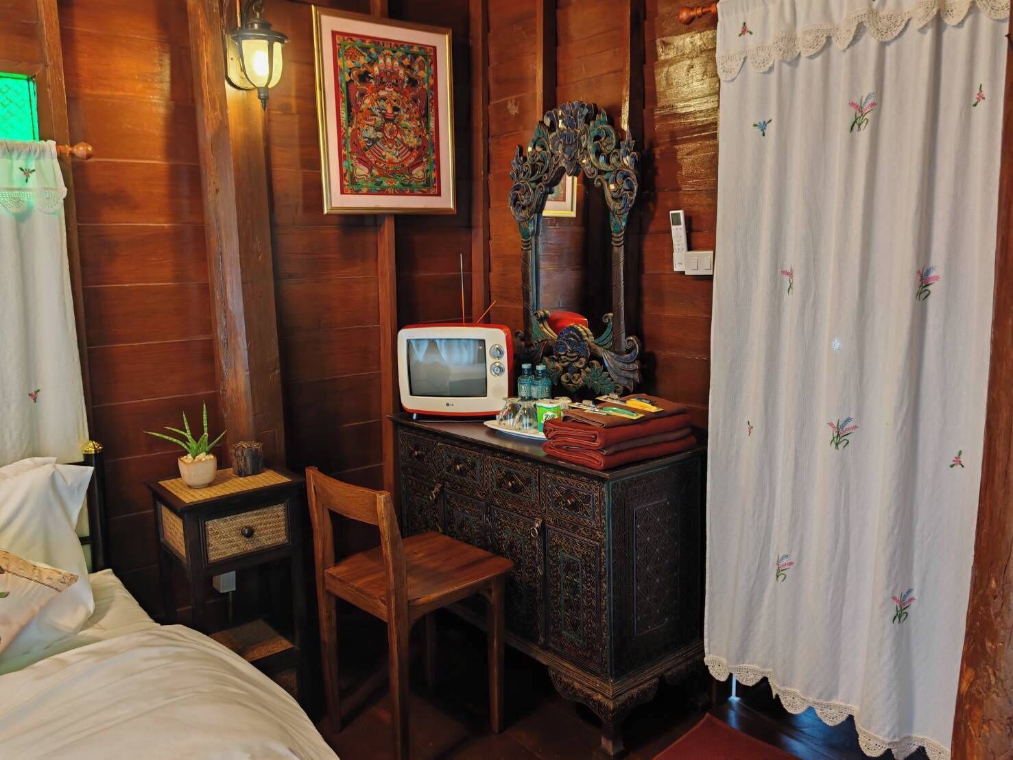 A traditional wooden room with a television, a decorative mirror, a small cabinet, and a chair.