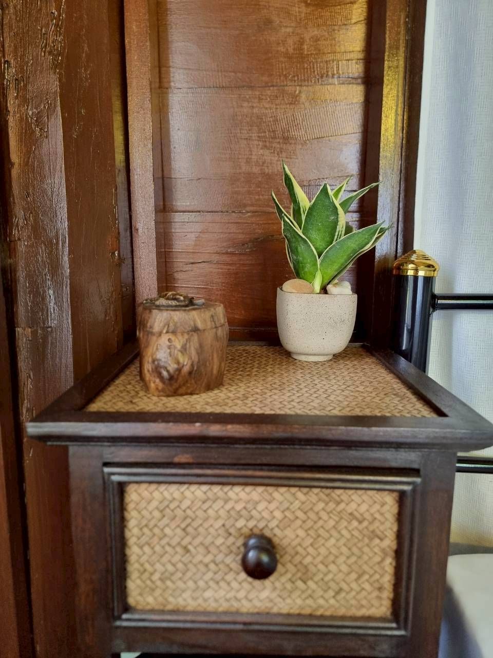 Een houten kastje met een geweven mat, een kleine plant en een decoratief houten object.