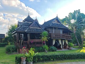 A traditional wooden house with a balcony, surrounded by lush greenery and tropical plants. - Huen Tip Viman Chiangmai (Doi Lo)