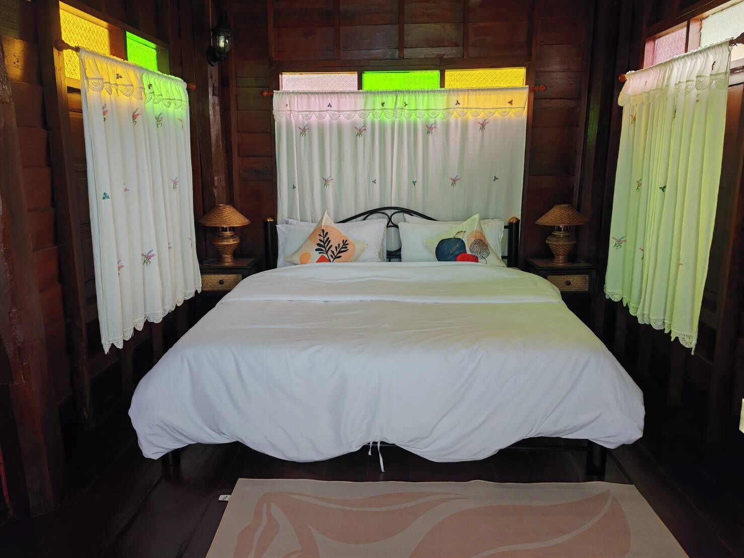 A neatly made bed with white bedding, two bedside lamps, and a window with green-tinted glass.