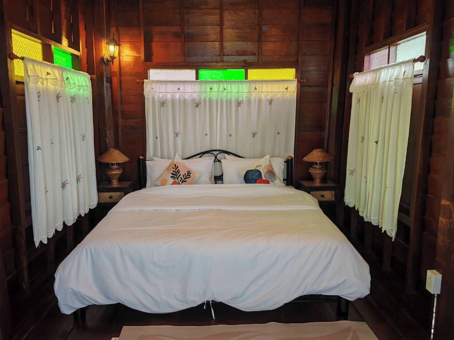 A wooden-paneled room with a bed, curtains, and two bedside lamps.