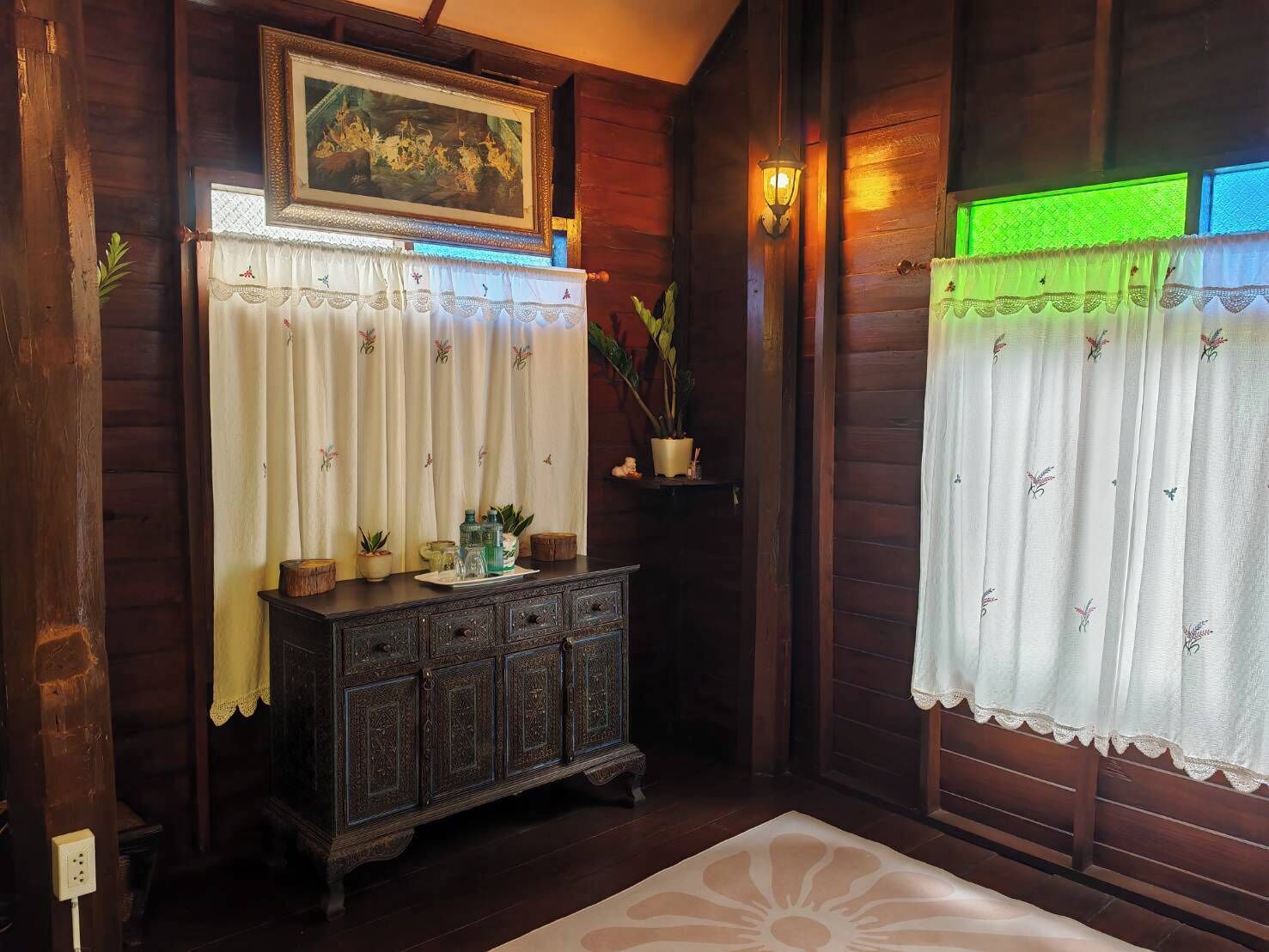 A room with wooden walls, a dark wooden cabinet, a painting above the cabinet, and a green light fixture.