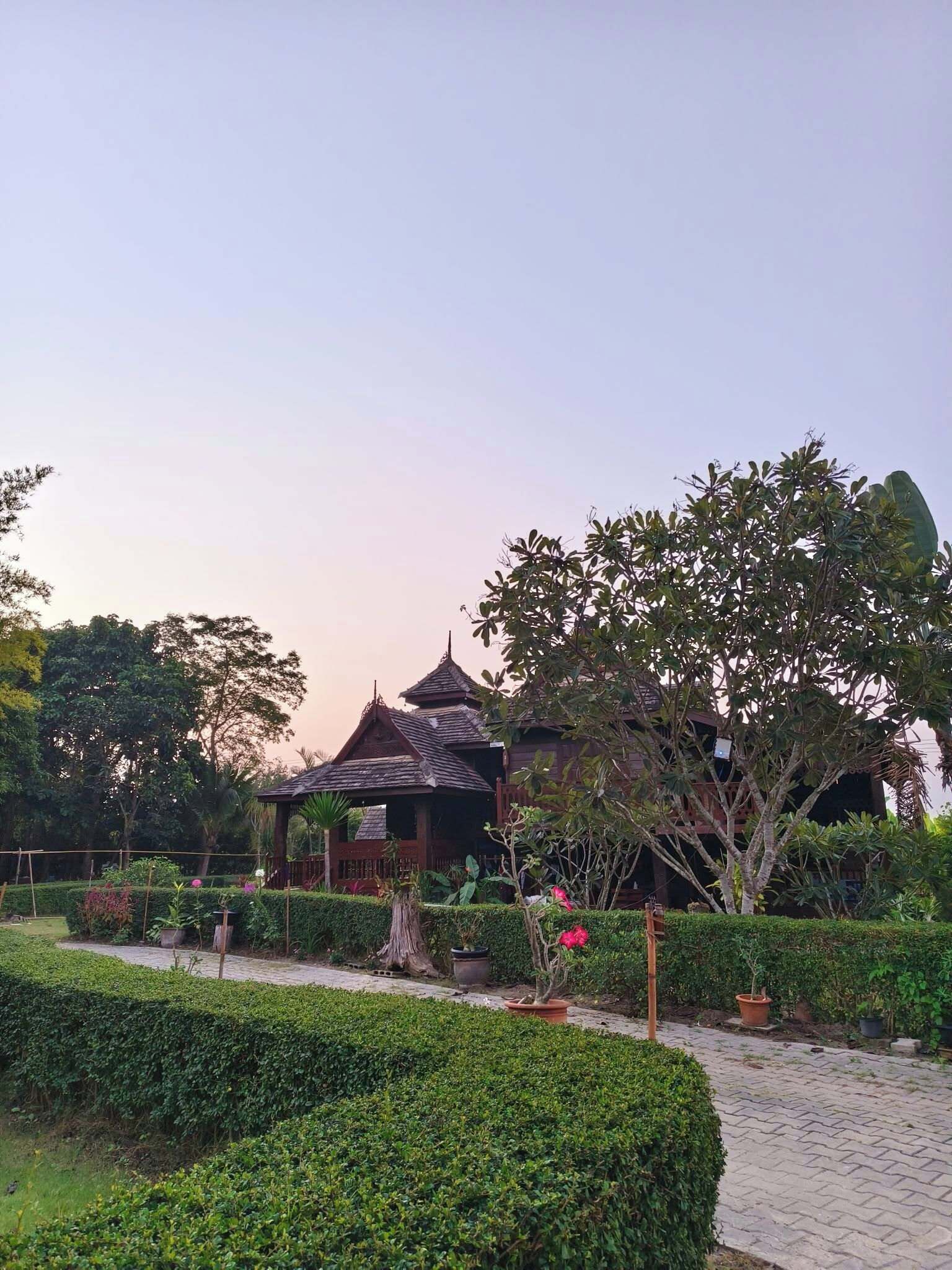 A traditional wooden building with a tiled roof, surrounded by well-maintained hedges and potted plants.