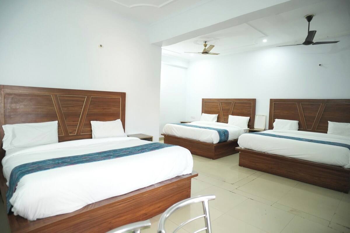 A hotel room with three wooden beds, white bedding, and a ceiling fan.