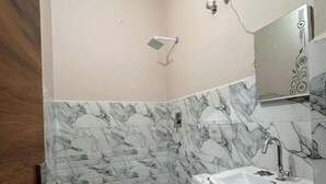 A bathroom with a marble backsplash, a toilet, a sink, and a hairdryer mounted on the wall. - Shree Hari palace (Vrindavan)