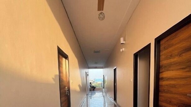 A long, narrow hallway with a ceiling fan, wooden doors on both sides, and a view of a garden at the end. - Shree Hari palace (Vrindavan)