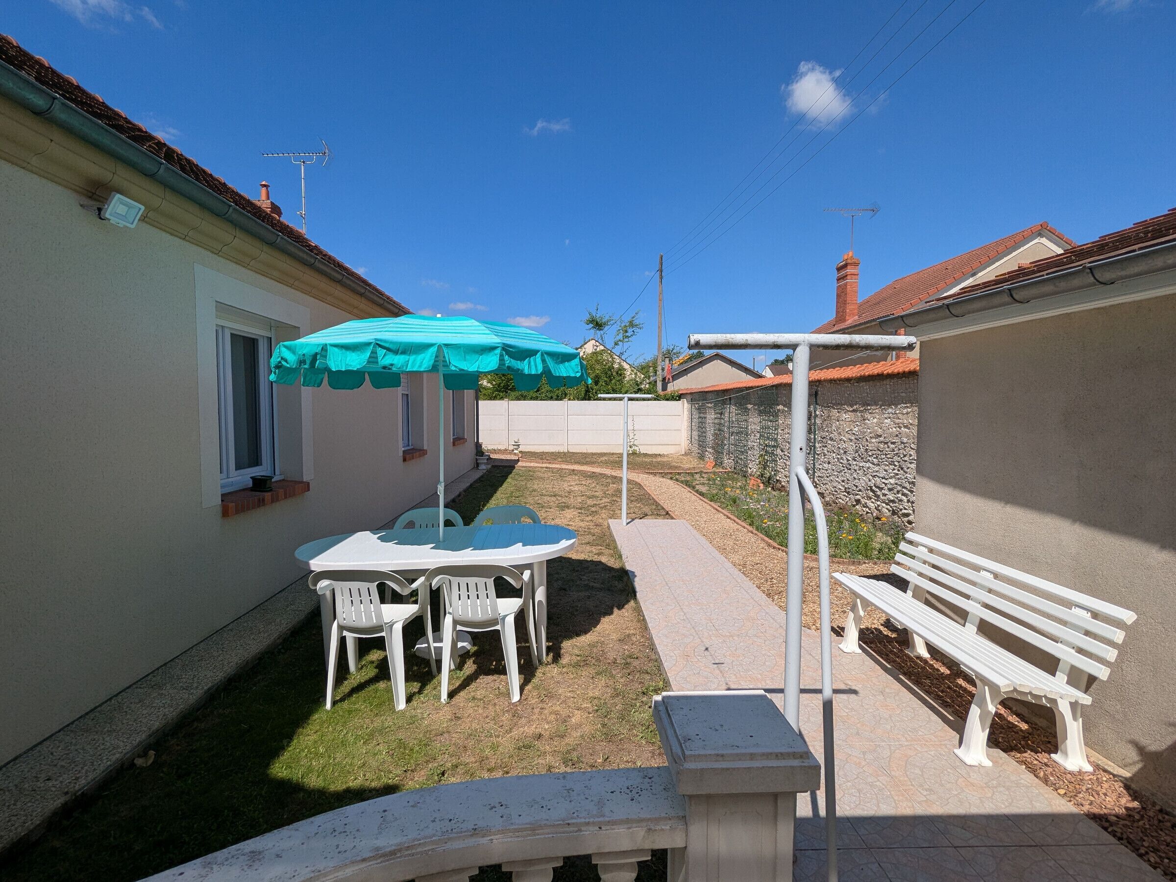 A patio with a table and chairs, a bench, and a turquoise umbrella.