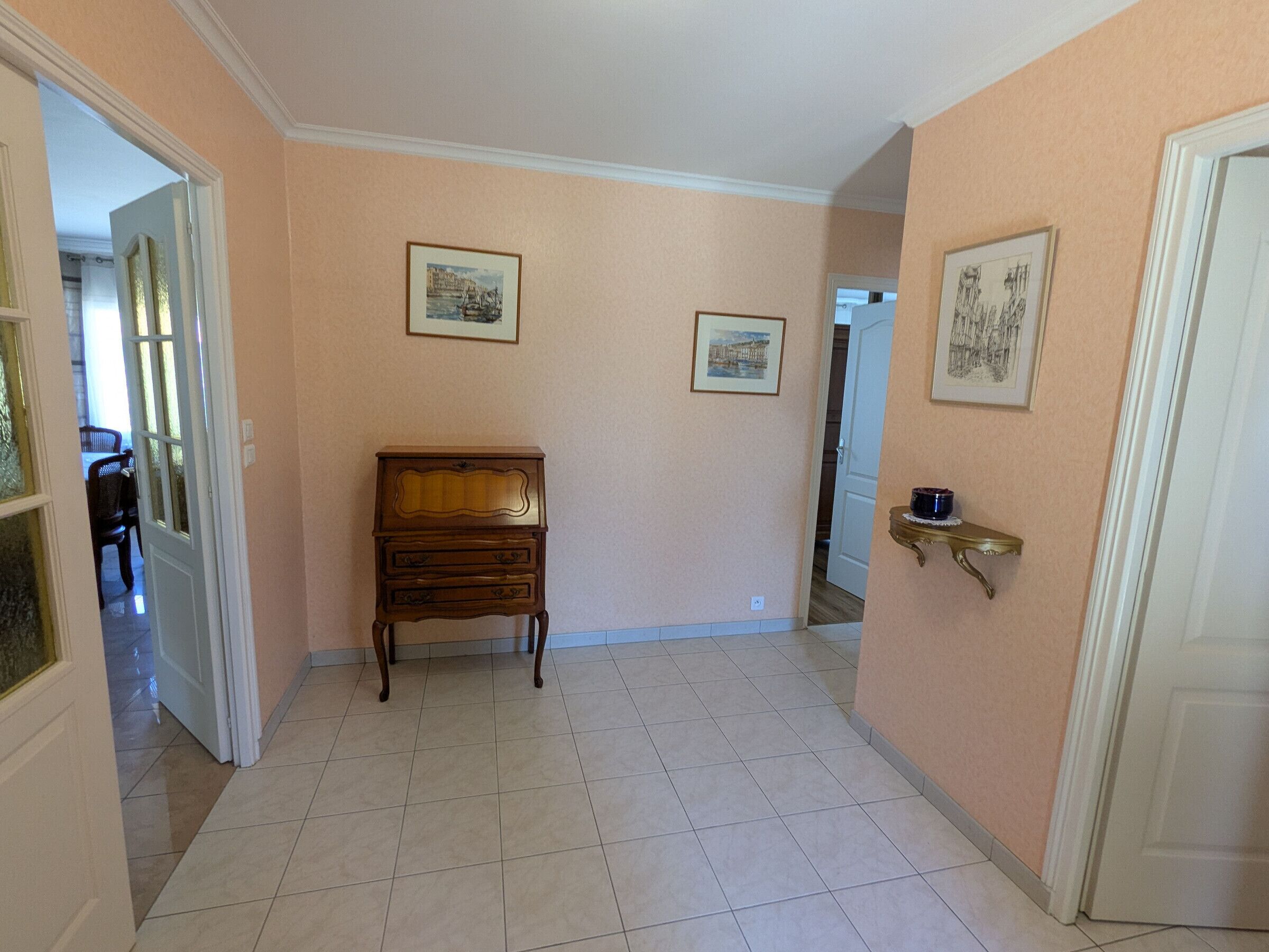 Un corridoio con un comò in legno, pavimento piastrellato e due quadri appesi alle pareti.