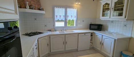 A kitchen with white cabinets, a black stove, a microwave, and a window with a curtain.