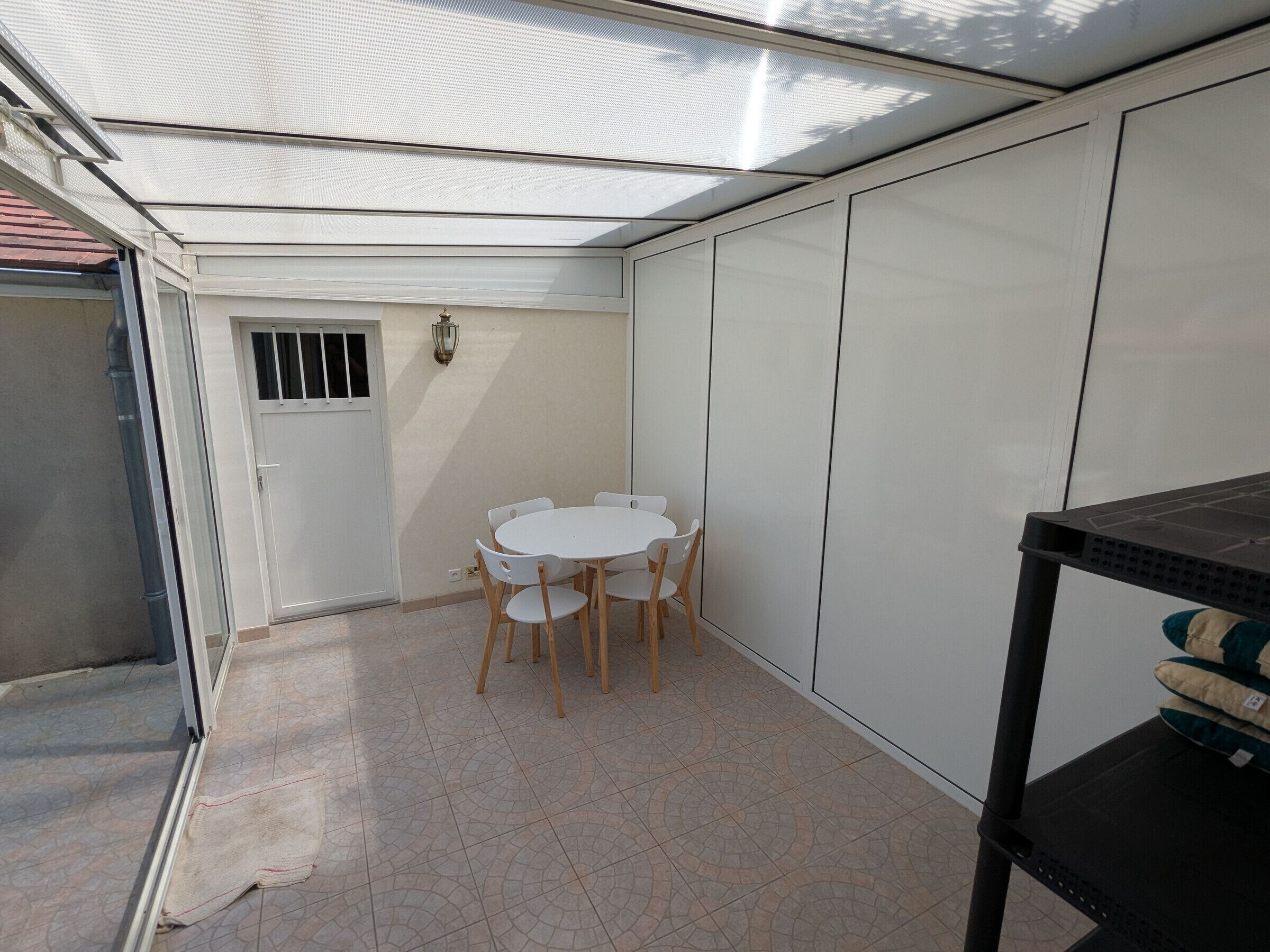Un piccolo patio con un tavolo rotondo e sedie, una porta e un muro con una finestra.