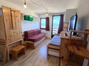 A compact room with a wooden bed, a sofa, a desk with a computer, and a TV.