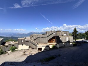 A modern building with a wooden exterior, multiple levels, and a view of mountains in the background. - Studio 3 pers, slopeside with balcony (Les Adrets-Prapoutel)