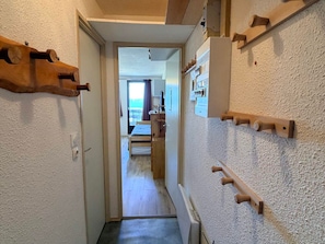 A narrow hallway with wooden wall-mounted hooks, a door leading to a room with a bed, and a view of a balcony. - Studio 3 pers, slopeside with balcony (Les Adrets-Prapoutel)