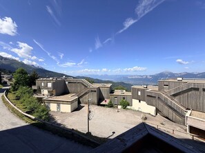 A modern building complex with multiple levels, a parking area, and a view of distant mountains.