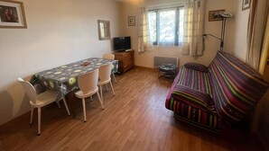 A compact living space with a dining table, chairs, a sofa, a television, and a window with curtains.