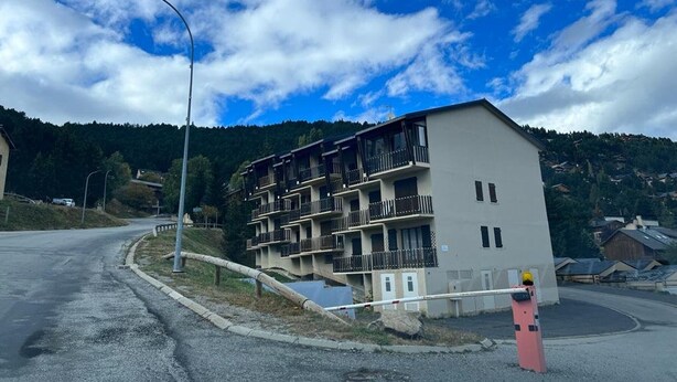 A multi-story building with balconies, a gated entrance, and a clear view of the surrounding landscape.