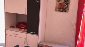 A small room with a table, chairs, a cabinet with a black panel, and a red object on the shelf. - Quiet Air-Conditioned Apartment with Parking Near Center and Beach for 4 (Cap d'Agde)