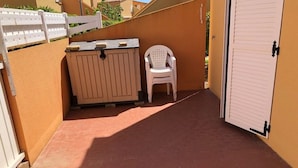 A small outdoor area with a white plastic chair, a beige storage unit, and a white door. - Quiet Air-Conditioned Apartment with Parking Near Center and Beach for 4 (Cap d'Agde)