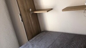 A corner of a room with a wooden cabinet, a gray textured bed, and a white wall. - Quiet Air-Conditioned Apartment with Parking Near Center and Beach for 4 (Cap d'Agde)