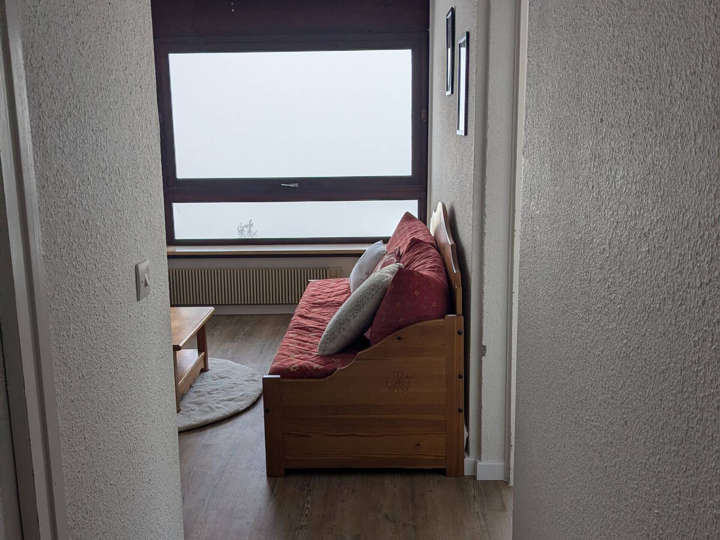 A small, cozy room with a wooden bed, a small table, and a window with a view of the sky.
