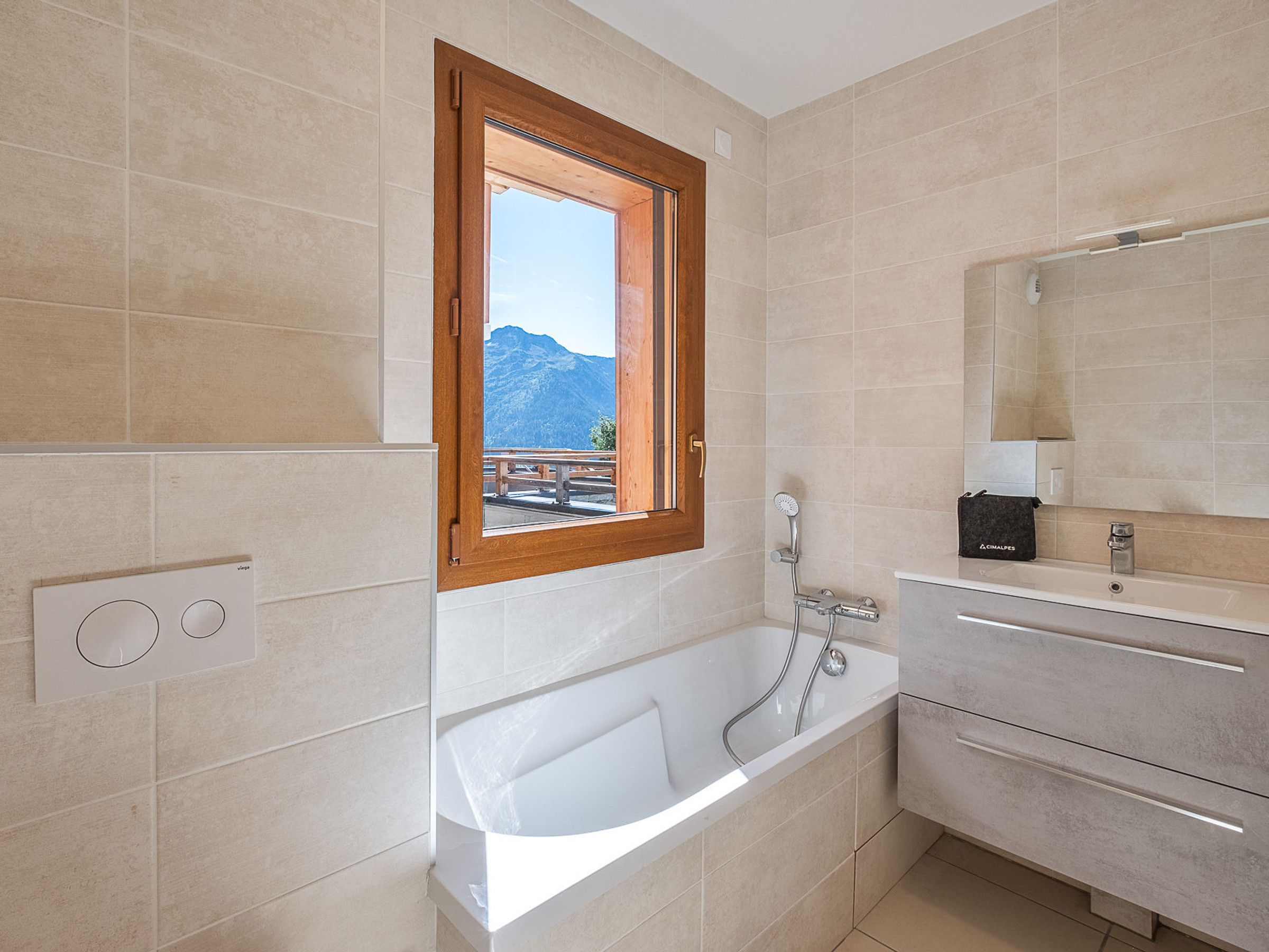 Een moderne badkamer met een bad, een raam met uitzicht op de bergen en een wastafel met spiegel.